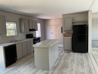 Kitchen with gray cabinetry, light wood-type flooring, black appliances, and a kitchen island