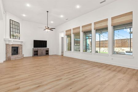Unfurnished living room with a brick fireplace, ceiling fan, and light wood-type flooring