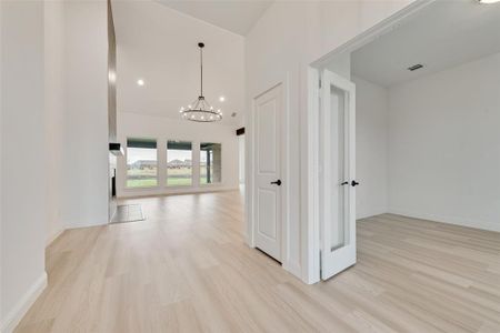 Corridor featuring light hardwood / wood-style flooring, an inviting chandelier, and a towering ceiling