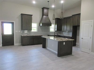 Kitchen with sink, custom exhaust hood, decorative backsplash, and a center island with sink