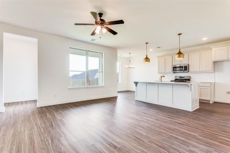 Kitchen featuring tasteful backsplash, hardwood / wood-style flooring, stainless steel appliances, ceiling fan with notable chandelier, and an island with sink