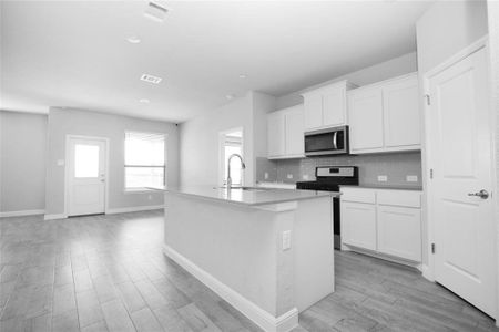 Kitchen featuring a kitchen island with sink, sink, stainless steel appliances, and white cabinets