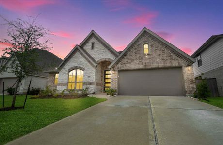 Charming single-story home featuring a striking brick facade, an inviting arched entryway, and a two-car garage, all set against a vibrant sunset sky.