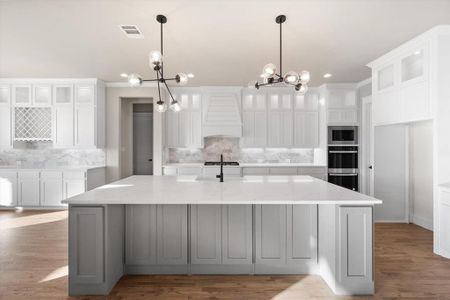 Kitchen with a large island, light hardwood / wood-style floors, white cabinets, light stone counters, and premium range hood