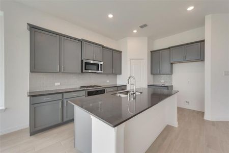 Kitchen featuring decorative backsplash, gray cabinetry, sink, appliances with stainless steel finishes, and a center island with sink