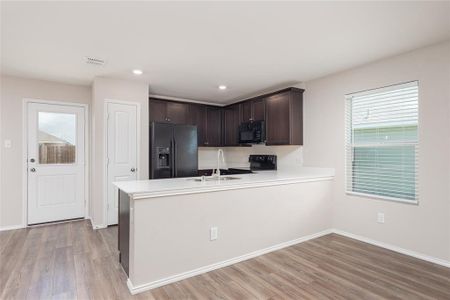 Kitchen with a healthy amount of sunlight, black appliances, light wood-type flooring, and kitchen peninsula