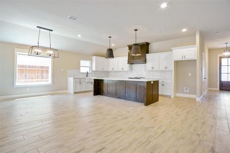 Kitchen with decorative light fixtures, white cabinetry, tasteful backsplash, a kitchen island, and light hardwood / wood-style floors