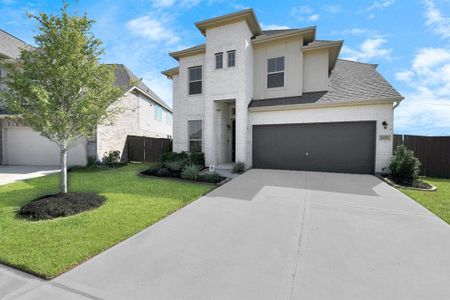 This is a modern two-story home featuring a brick facade, a two-car garage, and neatly landscaped front yard with a young tree and shrubbery. The property appears well-maintained, offering a clean and inviting suburban aesthetic.