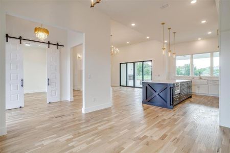 Kitchen featuring white cabinets, hanging light fixtures, a barn door, light wood-type flooring, and a center island