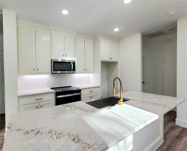 Kitchen with an island with a farmhouse styled sink, stainless steel appliances, gold fixtures, and light granite counters