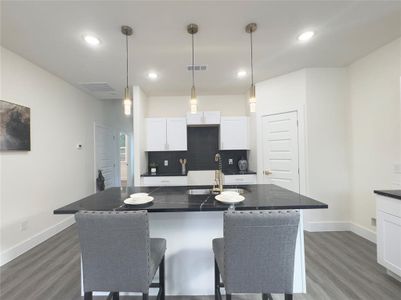 Kitchen featuring white cabinets, dark hardwood / wood-style flooring, sink, pendant lighting, and a center island with sink