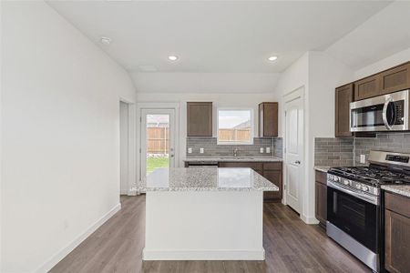 Kitchen featuring stainless steel appliances, wood-type flooring, vaulted ceiling, and a kitchen island