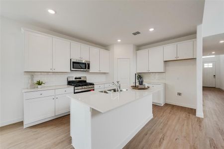 Kitchen featuring an island with sink, appliances with stainless steel finishes, white cabinetry, light wood-type flooring, and sink