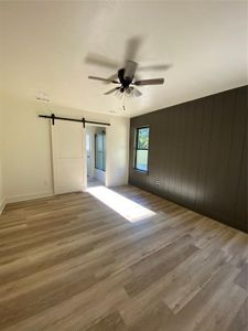 Unfurnished room featuring a barn door, ceiling fan, wood walls, and light wood-type flooring