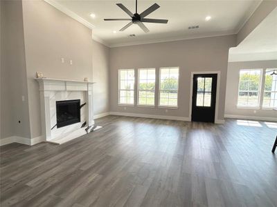 Unfurnished living room with a healthy amount of sunlight, crown molding, a high end fireplace, and dark hardwood / wood-style floors