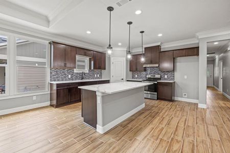 Kitchen with a center island, light stone countertops, stainless steel range with electric stovetop, decorative light fixtures, and tasteful backsplash
