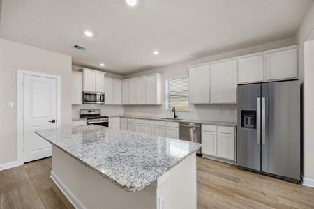 This beautifully designed kitchen features crisp white cabinets, a spacious island, sleek stainless steel appliances, and elegant granite countertops. The eye-catching herringbone tile backsplash adds a stylish finishing touch to this modern and functional space.