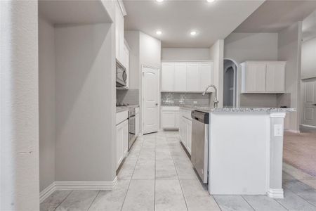 Kitchen featuring appliances with stainless steel finishes, white cabinetry, light tile patterned floors, and decorative backsplash