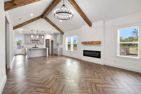 Unfurnished living room with a notable chandelier, lofted ceiling with beams, sink, and a healthy amount of sunlight