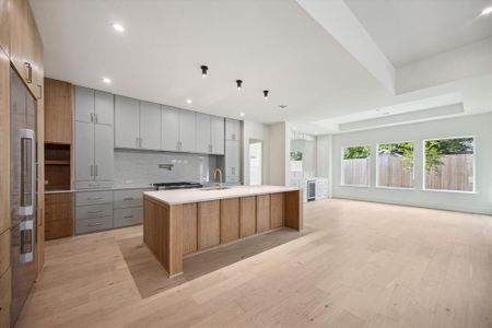 Contrasting soft grey cabinetry on the back wall of the large-scale kitchen creates depth and interest. Clean lines and brass hardware add a contemporary touch. Soft veining in the natural stone countertops brings everything together.