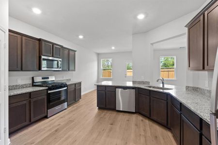 Kitchen featuring appliances with stainless steel finishes, light hardwood / wood-style flooring, sink, dark brown cabinetry, and light stone counters