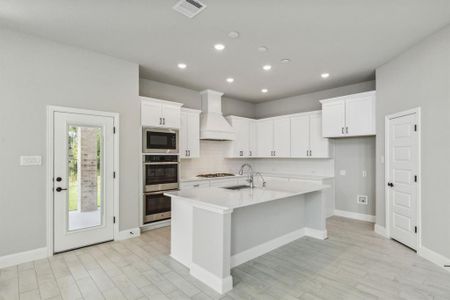 Kitchen with custom range hood, white cabinetry, sink, and a kitchen island with sink