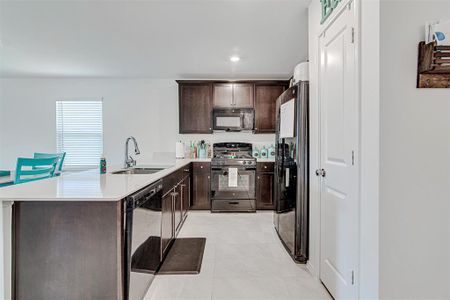 Kitchen featuring kitchen peninsula, light tile patterned floors, black appliances, dark brown cabinetry, and sink