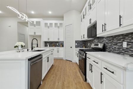 Kitchen with light hardwood / wood-style flooring, decorative light fixtures, stainless steel appliances, sink, and a center island with sink