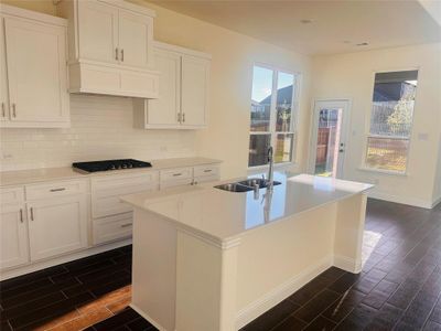 Kitchen featuring dark hardwood / wood-style floors, sink, white cabinets, a center island with sink, and gas stovetop