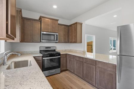 Kitchen with light wood-style floors, sink, kitchen peninsula, appliances with stainless steel finishes, and light stone countertops