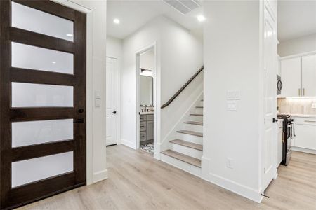 Enter a functional foyer featuring a guest bath and discreet stairs to a secondary living area. The open layout seamlessly connects to the first-floor living area, creating a welcoming space for daily living and entertaining.