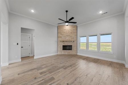 Unfurnished living room with a stone fireplace, crown molding, light wood-type flooring, and ceiling fan