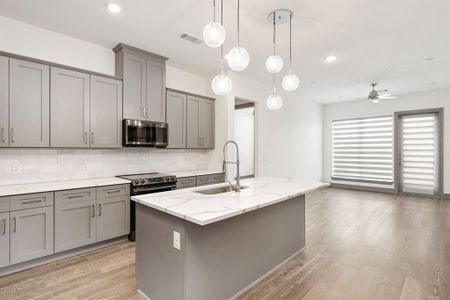 Kitchen featuring light hardwood / wood-style floors, appliances with stainless steel finishes, an island with sink, sink, and tasteful backsplash