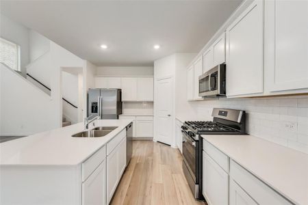 Kitchen featuring stainless steel appliances, tasteful backsplash, a kitchen island with sink, light wood-type flooring, and sink