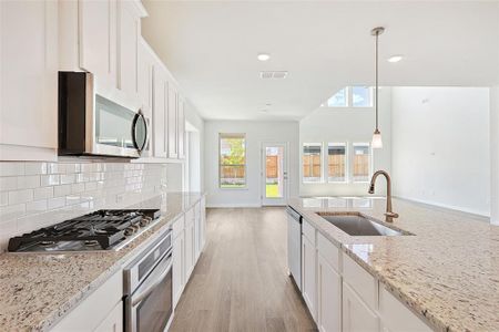 Kitchen with light wood-type flooring, tasteful backsplash, white cabinetry, appliances with stainless steel finishes, and sink