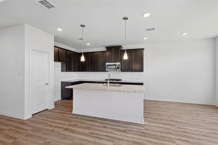 Kitchen featuring sink, decorative light fixtures, a center island with sink, and light wood-type flooring