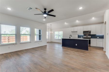 Kitchen with pendant lighting, light hardwood / wood-style floors, a kitchen island with sink, white cabinets, and appliances with stainless steel finishes