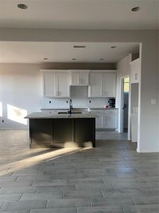 Kitchen featuring an island with sink, light stone counters, sink, white cabinetry, and backsplash