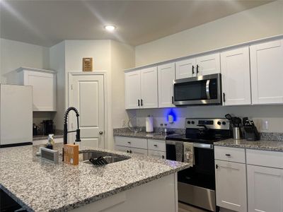 Kitchen featuring appliances with stainless steel finishes, white cabinetry, a kitchen island with sink, light stone countertops, and sink