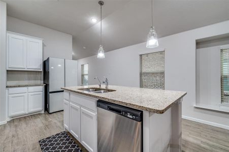 Kitchen with dishwasher, a center island with sink, white cabinetry, and hanging light fixtures