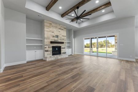 living room with ceiling fan, beamed ceiling, built in shelves, and a stone fireplace