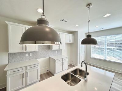 Kitchen featuring hanging light fixtures, sink, light hardwood / wood-style floors, white cabinets, and backsplash