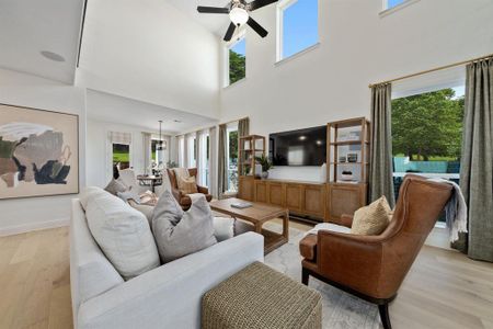 Living room featuring a healthy amount of sunlight, a towering ceiling, light hardwood / wood-style flooring, and ceiling fan with notable chandelier