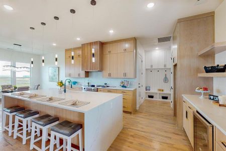 Kitchen featuring high end stainless steel range oven, light hardwood / wood-style floors, wine cooler, a kitchen breakfast bar, and a kitchen island with sink