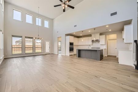 Unfurnished living room with light hardwood / wood-style floors, a towering ceiling, sink, and ceiling fan with notable chandelier