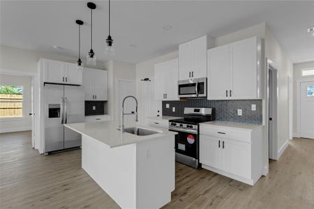 Kitchen featuring white cabinetry, pendant lighting, stainless steel appliances, a center island with sink, and sink