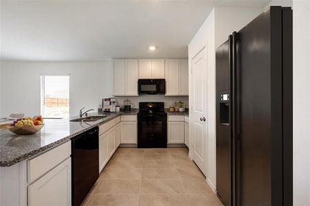 Kitchen featuring dark stone counters, light tile flooring, white cabinetry, black appliances, and sink