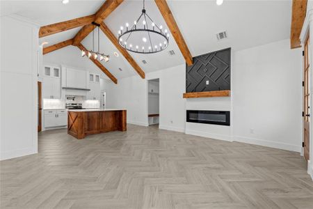 Kitchen with a kitchen island with sink, light parquet floors, decorative light fixtures, white cabinets, and high vaulted ceiling