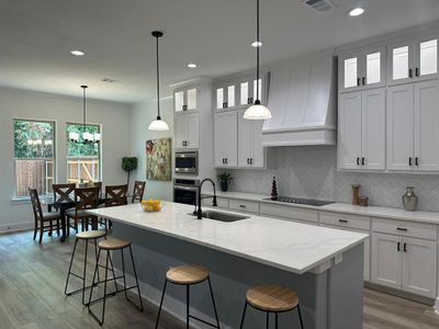 Kitchen featuring decorative light fixtures, wood-type flooring, sink, custom range hood, and a kitchen island with sink