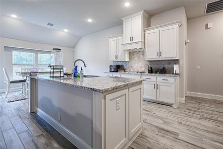 Kitchen featuring light stone countertops, sink, white cabinetry, light hardwood / wood-style floors, and a center island with sink